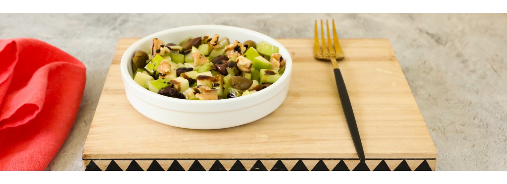 Una fresca insalata di mele e sedano, con olive e noci tritate, è condita con una glassa di aceto balsamico e servita in maniera minimal ed elegante