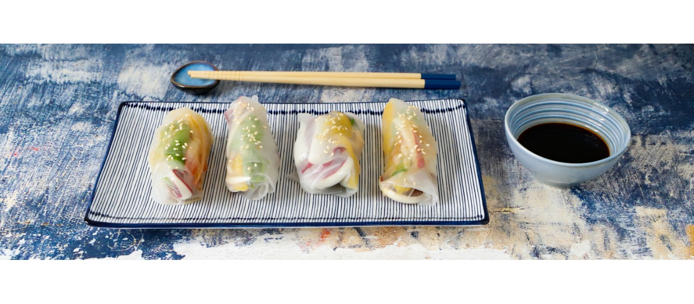 Involtini di carta di riso colorati serviti su un piatto smaltato a righe, accompagnati da salsa di soia e bacchette