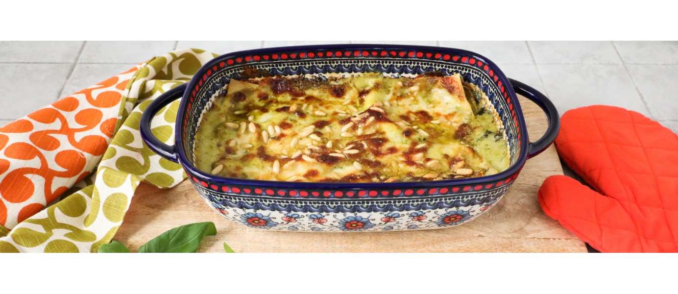 In una coloratissima terrina sono servite delle golose lasagne al pesto decorate con i pinoli, appoggiata su un tagliere