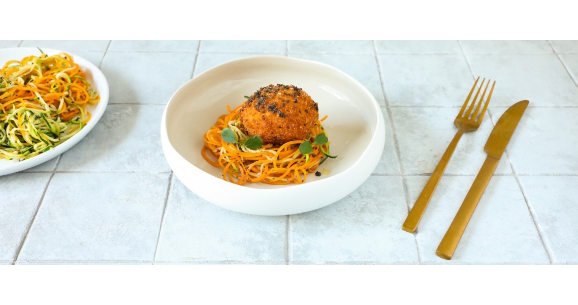 Su un piatto tondo è servito un nido di spaghetti di zucchine e carote, su cui è poggiato un uovo impanato e fritto, con una profumata salsa tartufata