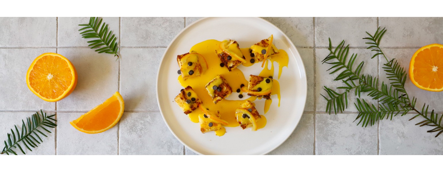Su un piatto bianco, una composizione gourmet di fette di pandoro tostate, una dorata crema di zabaione, scorzette d’arancia e cioccolato