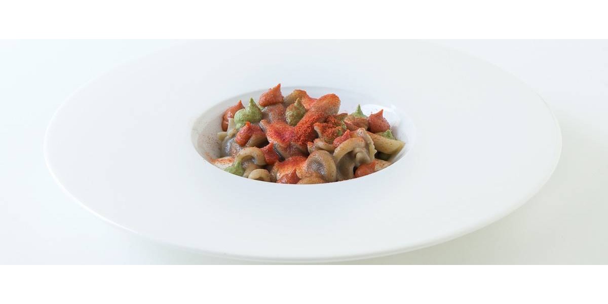 Nel piatto si vede la pasta resa rossa dalla crema di condimento, con ciuffi di pomodoro e basilico