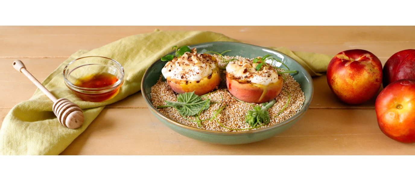 Pesche grigliate e farcite di crema di ricotta, decorate con nocciole, miele e cioccolato grattugiato, servite su un piatto decorato come una spiaggia in estate