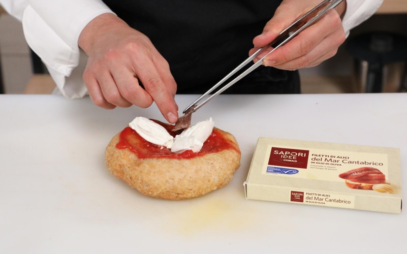 Condire la pizza fritta con salsa di pomodoro, quenelle di ricotta e alici