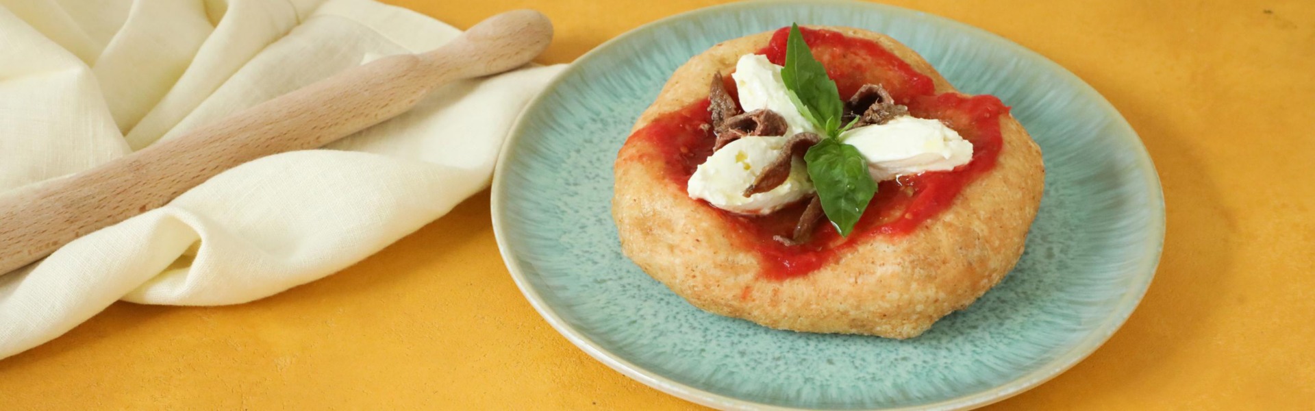 Una pizza fritta è servita su un piatto colorato, farcita salsa di pomodoro, quenelle di ricotta e filetti di alici