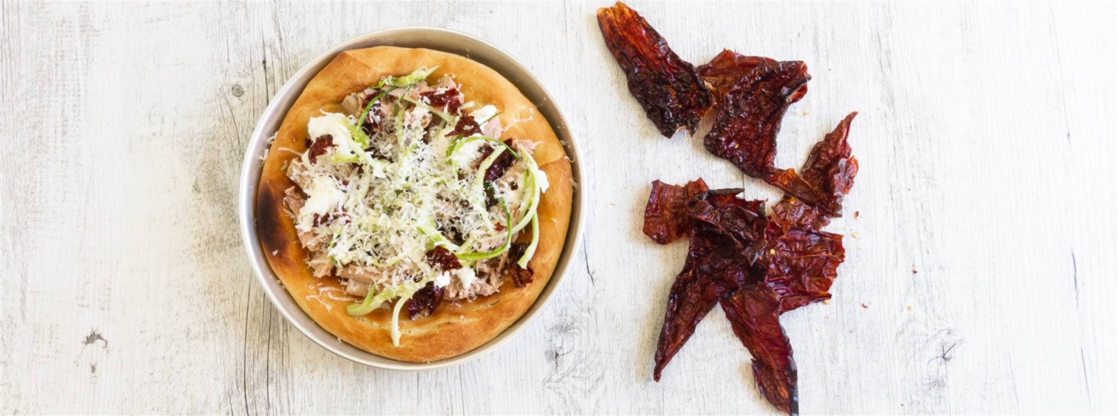 Pizza con tonno e rosso peperone crusco ricoperta da scaglie di formaggio bianco su tavola bianca