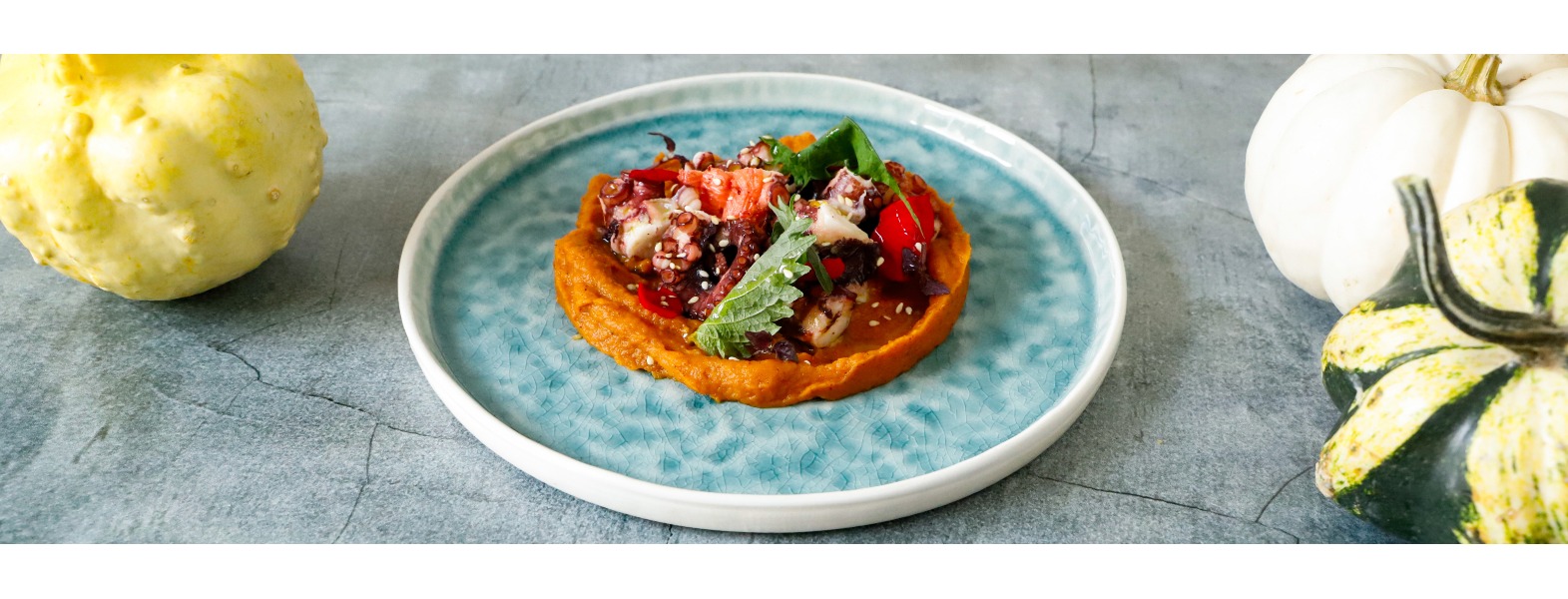 Polpo lessato servito su letto di crema di zucca, in contrasto con il piatto azzurro