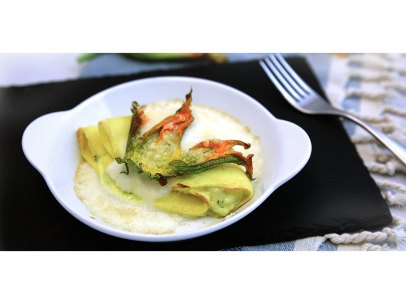 Crespelle verdi chiuse a ventaglio e decorate con un fiore di zucca, leggermente gratinate e servite all’interno di una cocottina 