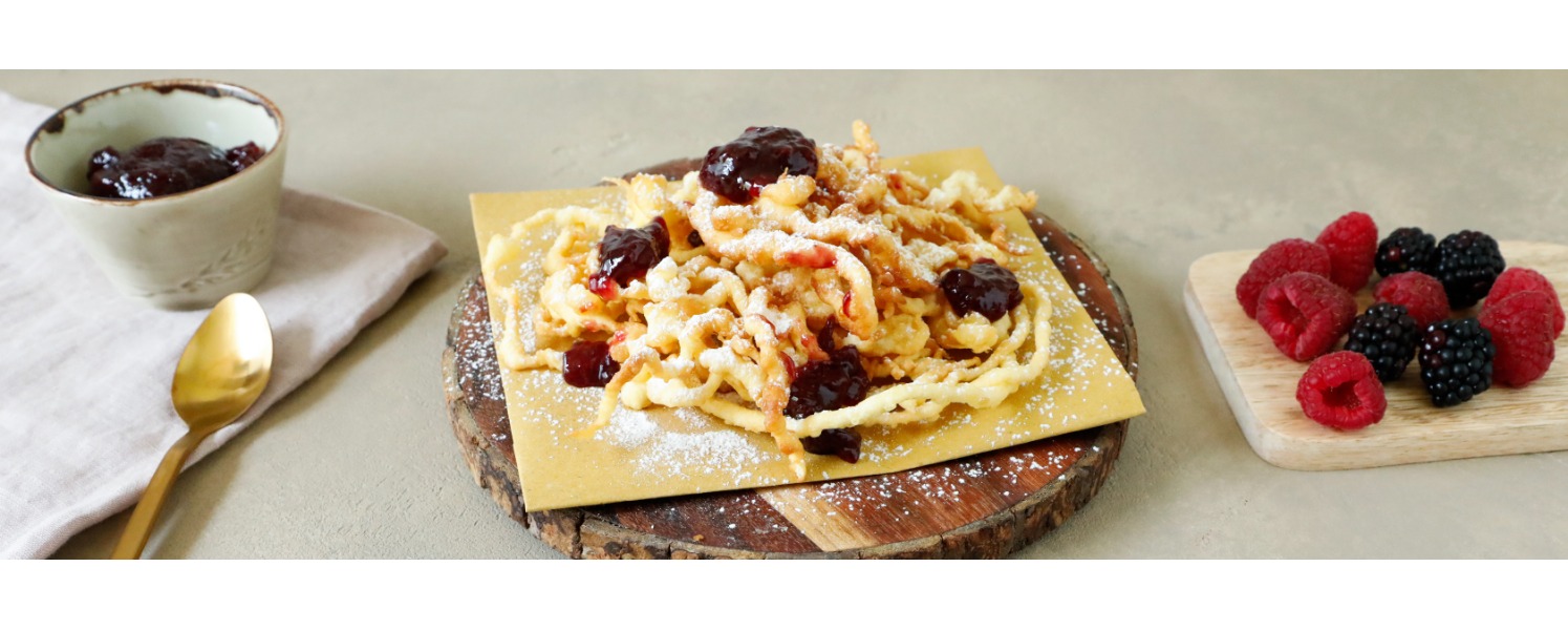 Croccanti frittelle tipiche tirolesi servite su un tagliere di legno con confettura di frutti di bosco e una spolverata di zucchero a velo