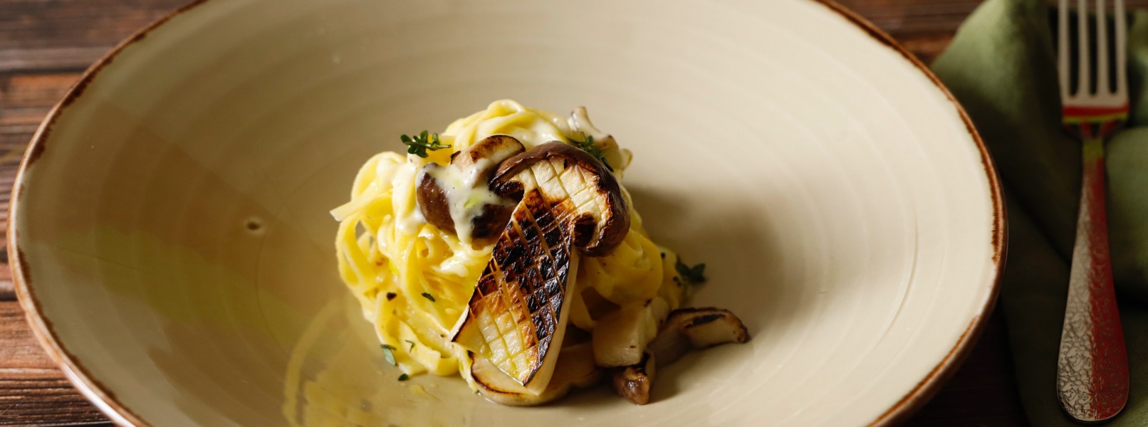 Tagliatelle ai funghi con crema d'aglio e olio al dragoncello in un piatto bianco al centro di un tavolo