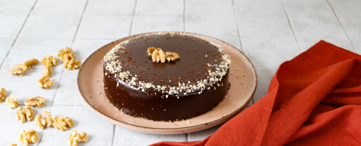 La torta di noci e scaglie di cioccolato è servita su un piatto, con una glassa a specchio lucente e decorata con noci tritate e scaglie di cioccolato fondente