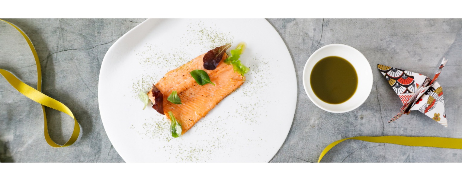 Il filetto di trota è servito su un piatto bianco con una salsa al tè matcha e foglioline di insalata