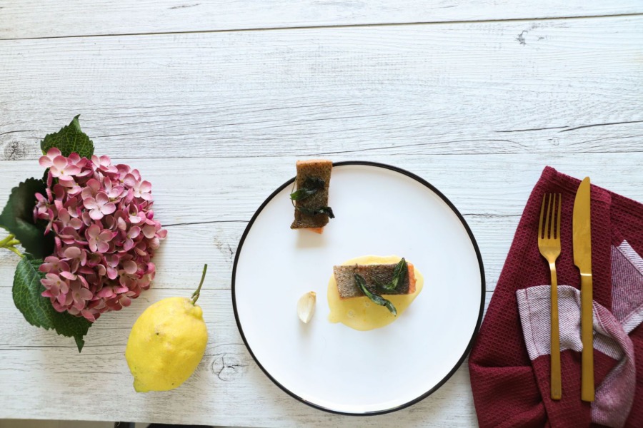 I filetti di trota scottata sono serviti con una gialla crema di limoni e foglioline di prezzemolo, serviti a tavola con fiori primaverili