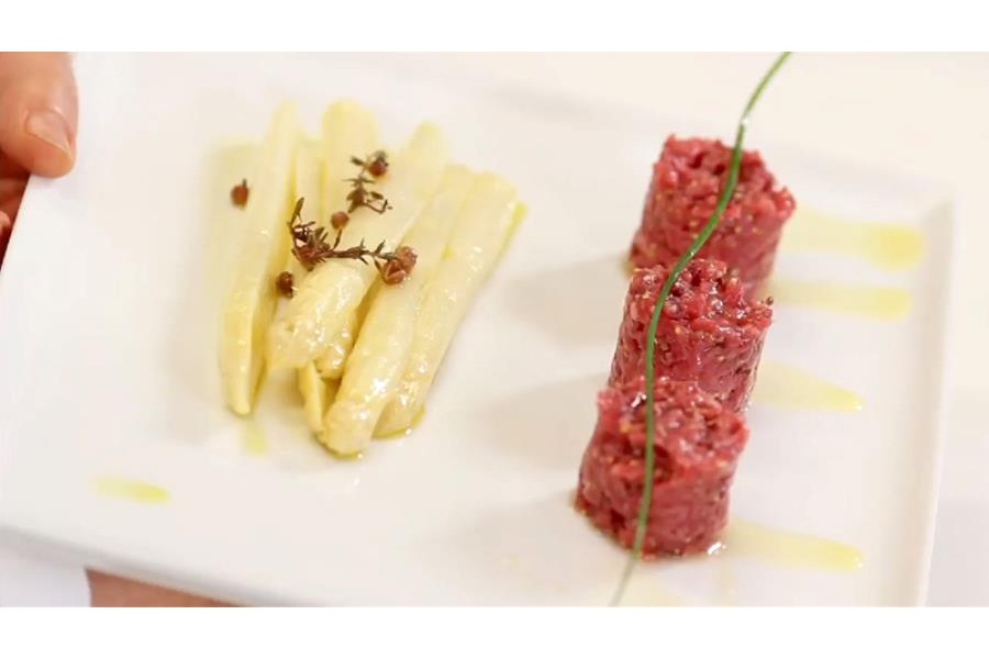 La battuta di manzo è adagiata su un elegante piatto bianco, servita con asparagi bianchi