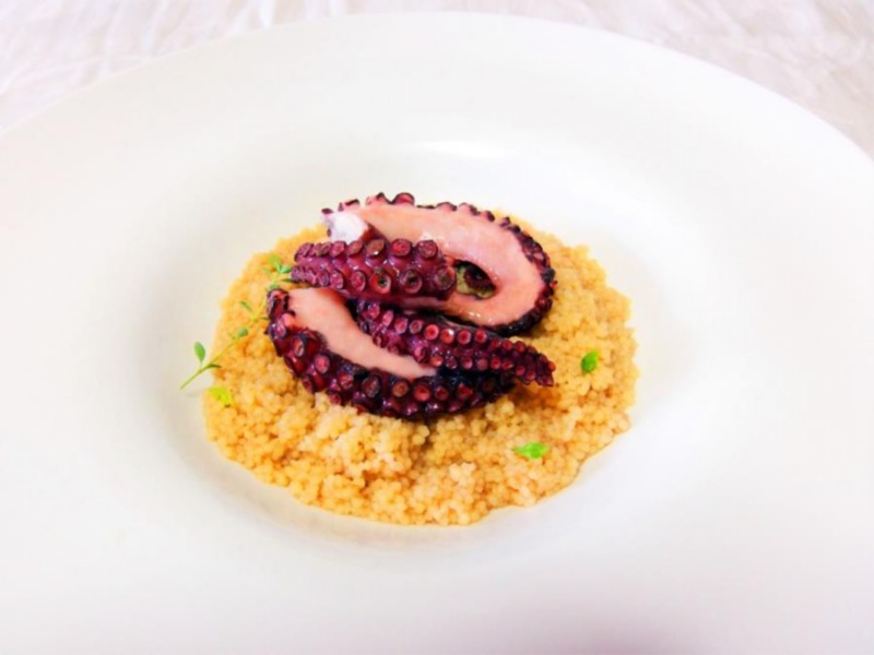 Su un elegante piatto bianco è servito un dorato cous cous con carnosi tentacoli di polpo 