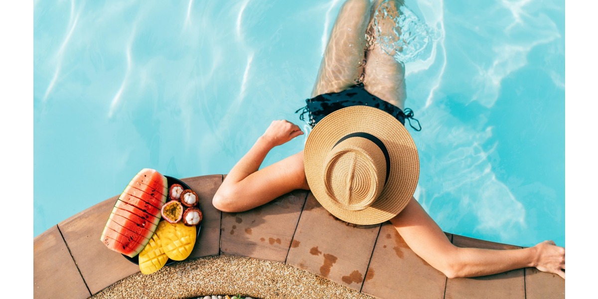 Una ragazza prende il sole a bordo piscina con al suo fianco alcuni cibi da mangiare in estate per l'abbronzatura
