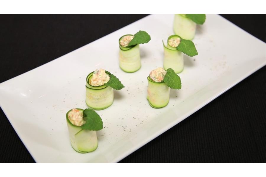 Su un piatto bianco sono serviti degli eleganti involtini di zucchine crude con un ripieno di cremoso formaggio alle carote