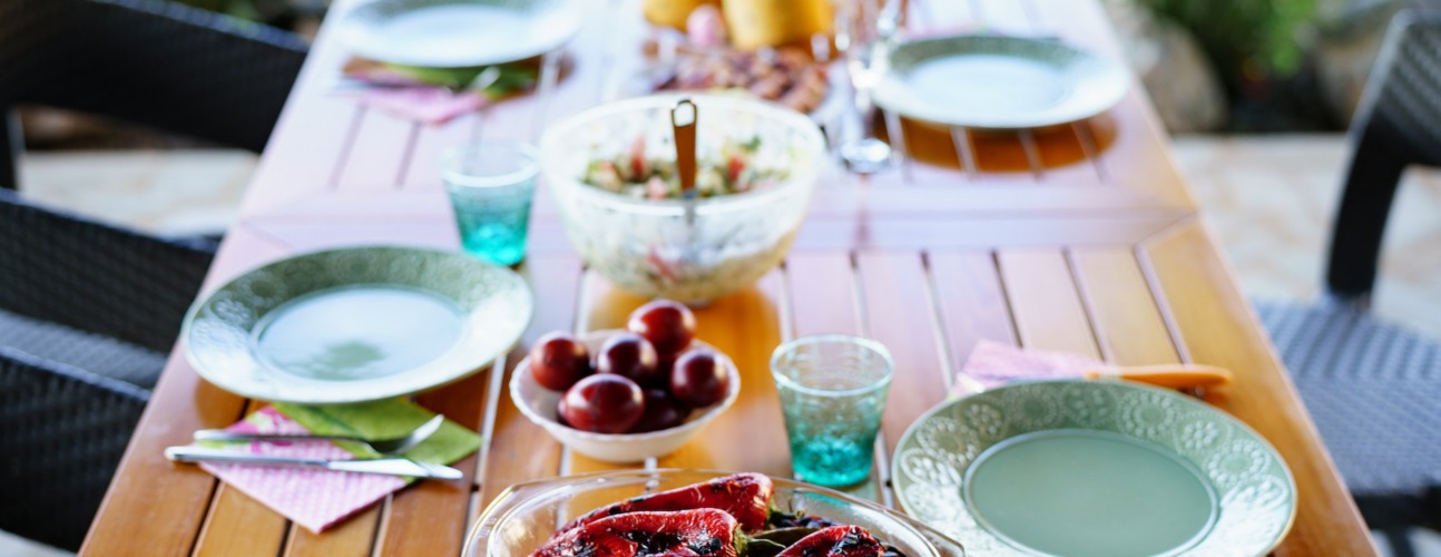 Una tavola in legno presenta piatti e bicchieri verdi, pronta ad accogliere le pietanze del Menu di Primavera