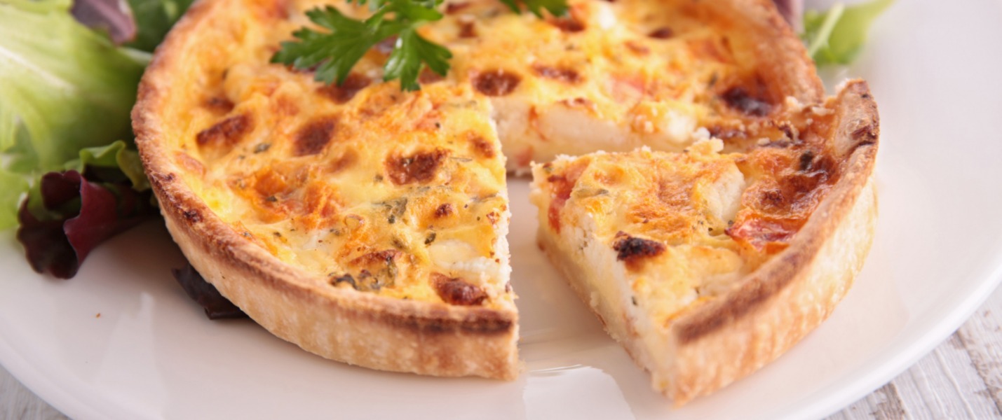 Torta salata con pancetta, uova e formaggio su un piatto bianco con insalata