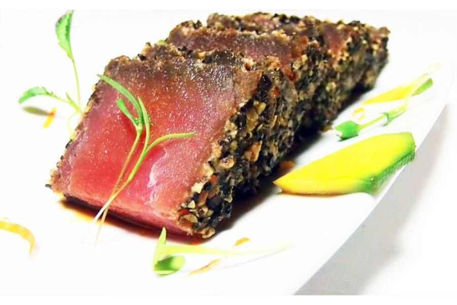 Su un piatto bianco è servito il sashimi di tonno rosso ricoperto da una panure di pepe nero e bianco