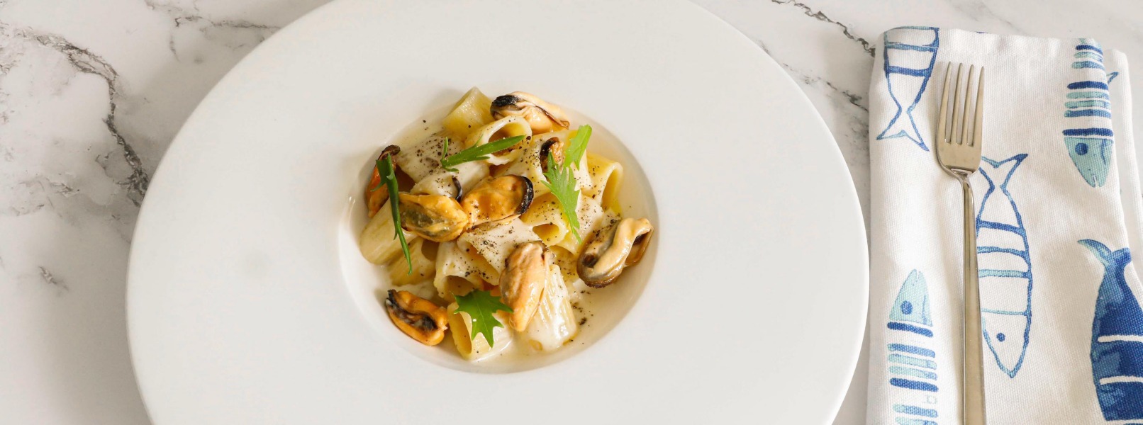 In un piatto bianco sono presentate le mezze maniche con cozze, condite con cacio e pepe. Una presentazione estiva che sa di vacanze al mare