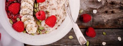 La ciotola di porridge nel dettaglio con avena e lamponi e banane su un tavolo di legno