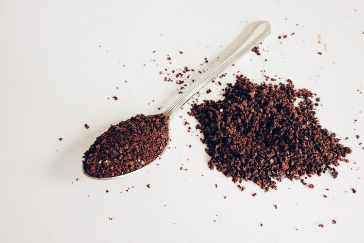 Colher com pó de café, e um punhado de café esparramado ao lado.