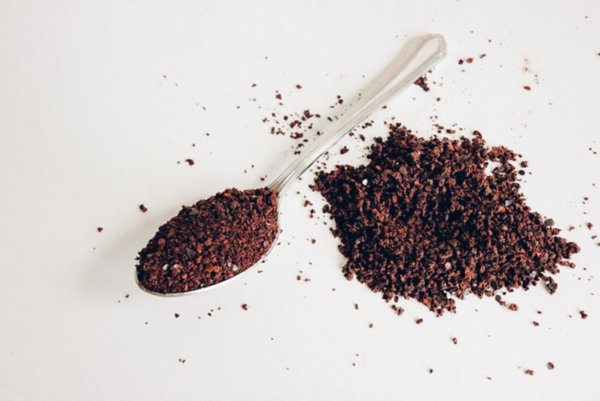 Colher com pó de café, e um punhado de café esparramado ao lado.